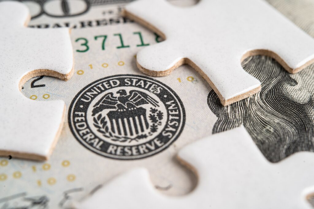 U.S. dollar bill overlaid with Federal Reserve emblem and puzzle pieces, symbolizing monetary policy challenges and economic uncertainty.