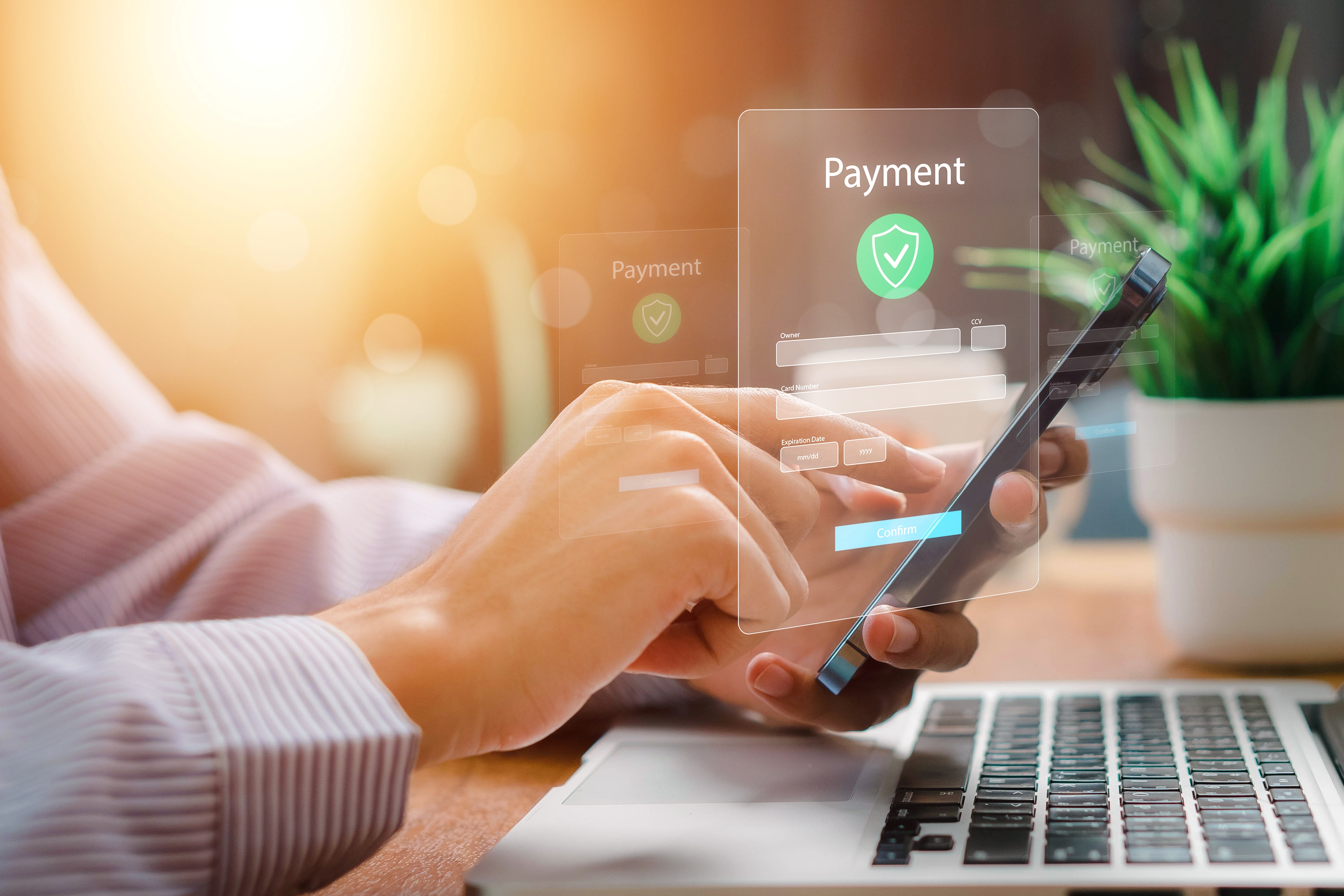 Person completing an online payment on a smartphone with a secure digital interface displayed above a laptop.